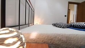 A bedroom with a bed, a wooden nightstand, a patterned pillow, and a door leading to another room.
