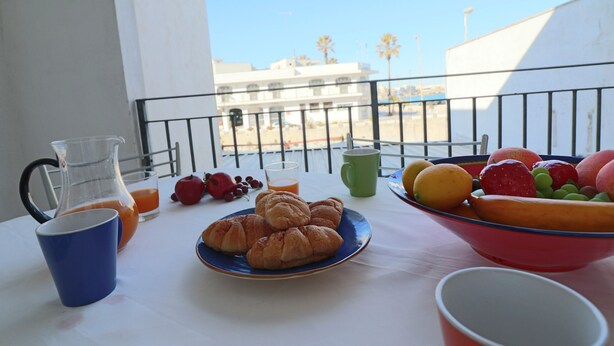 A balcony with a table set for breakfast, including croissants, fruit, and juice.