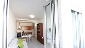 A room with a bed, a dining table with chairs, a kitchen area, and a sliding glass door leading to an outdoor area.