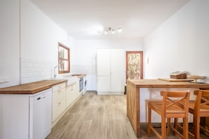 Eine Küche mit weißen Schränken, einer Holzausziehtafel, einer Waschmaschine und einem Essbereich mit Holzkufen.