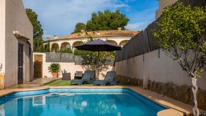 Una piscina con sillones de descanso, una pérgola y vistas a un edificio con arcos.