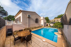 A swimming pool with a table and chairs, a building with a sloped roof, and a stone wall. - Typical Majorcan town house with pool – Casa Manolo (Cala Ratjada)