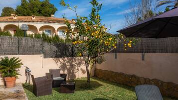 Un patio con mobiliario de mimbre, un árbol con flores amarillas y un muro de piedra.