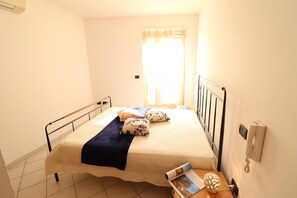 A single bed with a headboard, a bedside table with a lamp, a telephone, and a window with curtains.