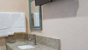Un baño con lavamanos de encimera de granito, un espejo y un televisor montado en la pared.