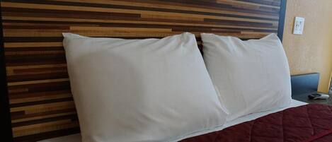 A bed with white pillows and a red blanket, against a wooden headboard.
