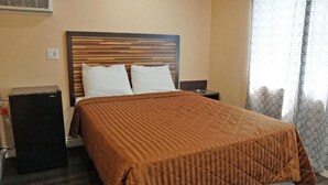 Una habitación de hotel con una cama, una mesita de noche, un calentador pequeño y una ventana con cortinas estampadas.