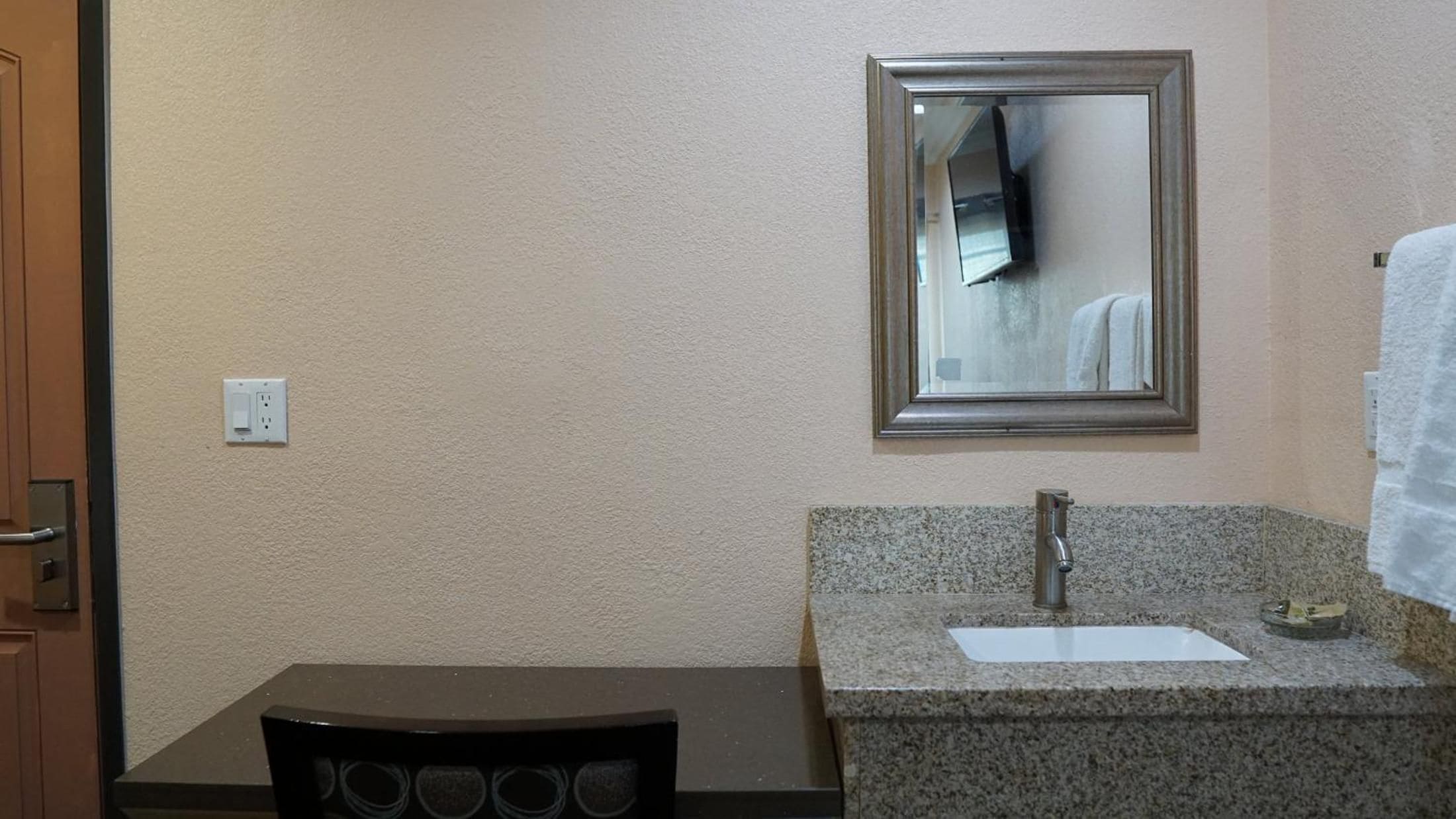 A bathroom with a granite countertop, a sink, a mirror, and a towel rack.