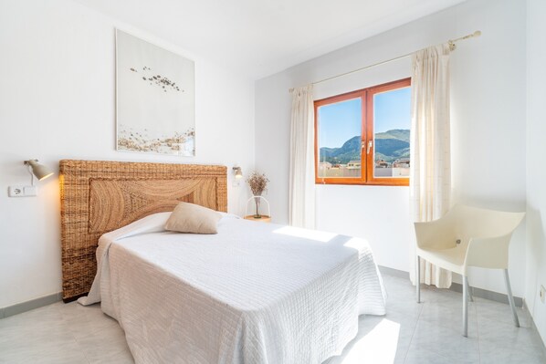A bedroom with a bed, a chair, a window with a view, and a wall-mounted artwork.