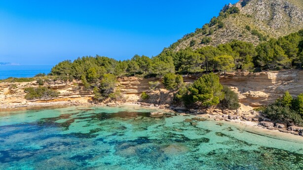 Un paysage côtier caractérisé par des eaux turquoise limpides, un terrain rocheux et une végétation luxuriante.
