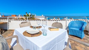 Une table dressée pour deux personnes, avec vue sur la mer, des places assises en plein air et une balustrade blanche.