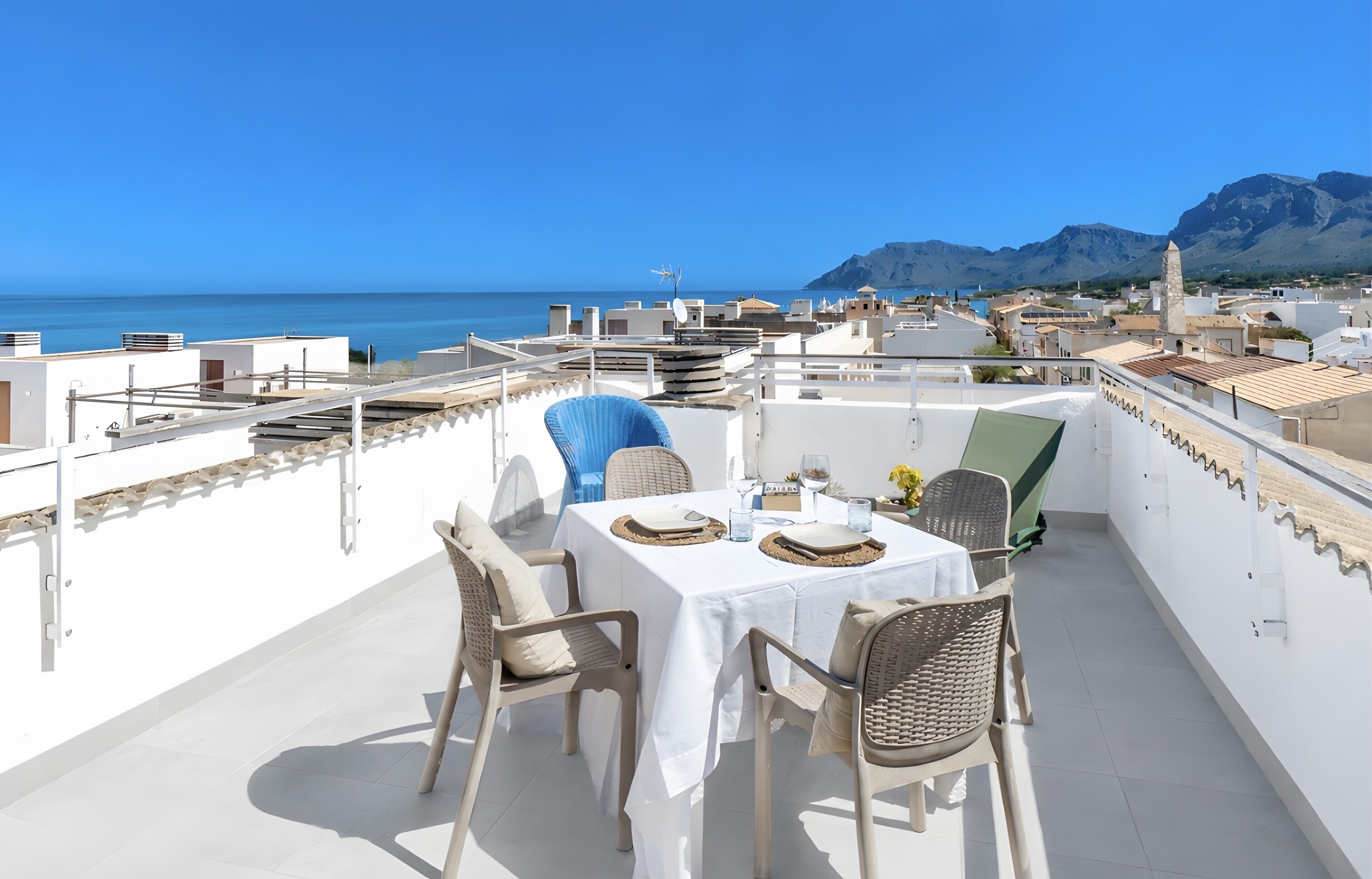 Terraza en la azotea con una mesa lista para comer, sillas y vistas al mar y a las montañas.