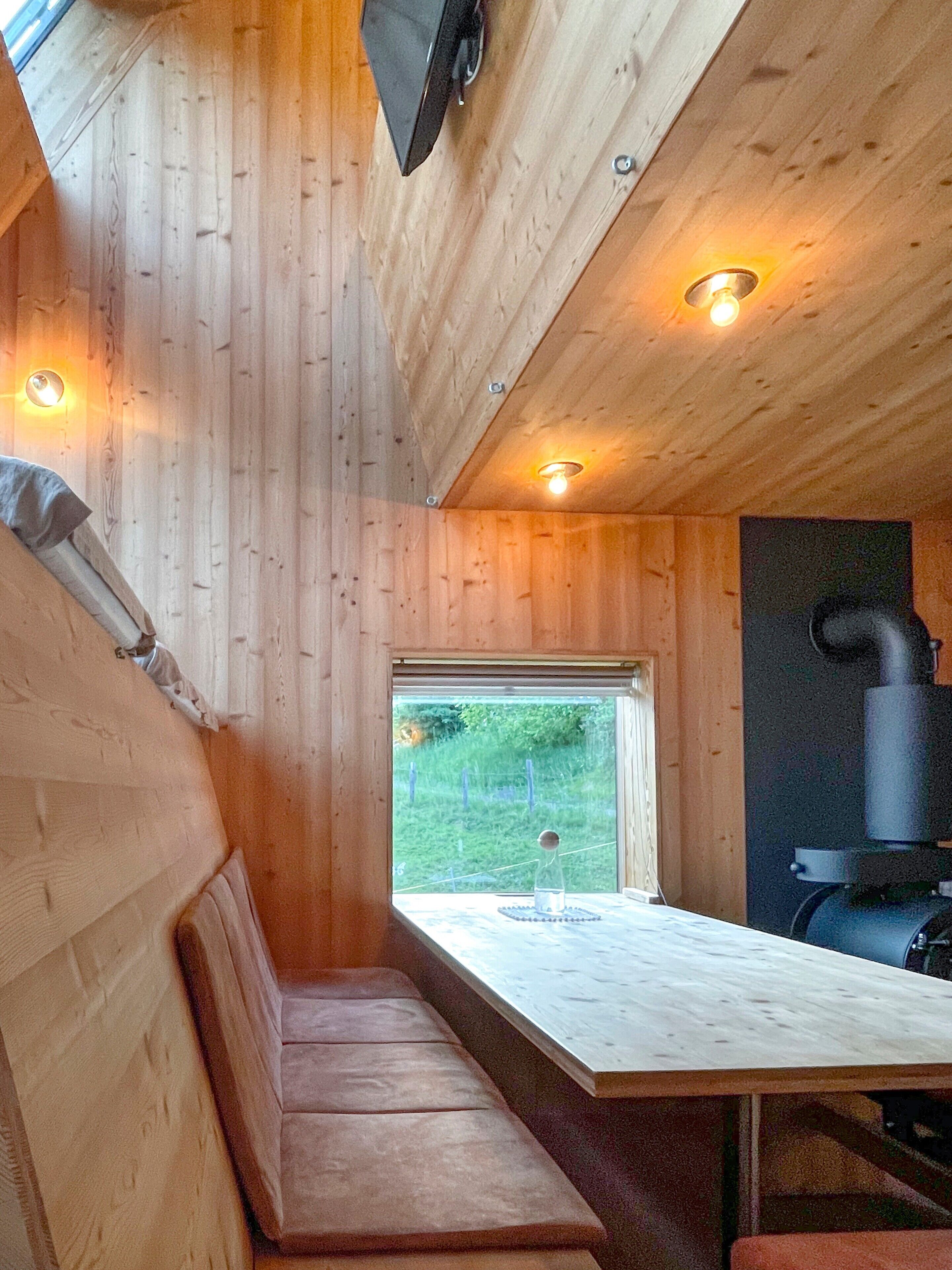 L’intérieur d’une cabane en bois, avec un banc, une table, une fenêtre et un poêle à bois.
