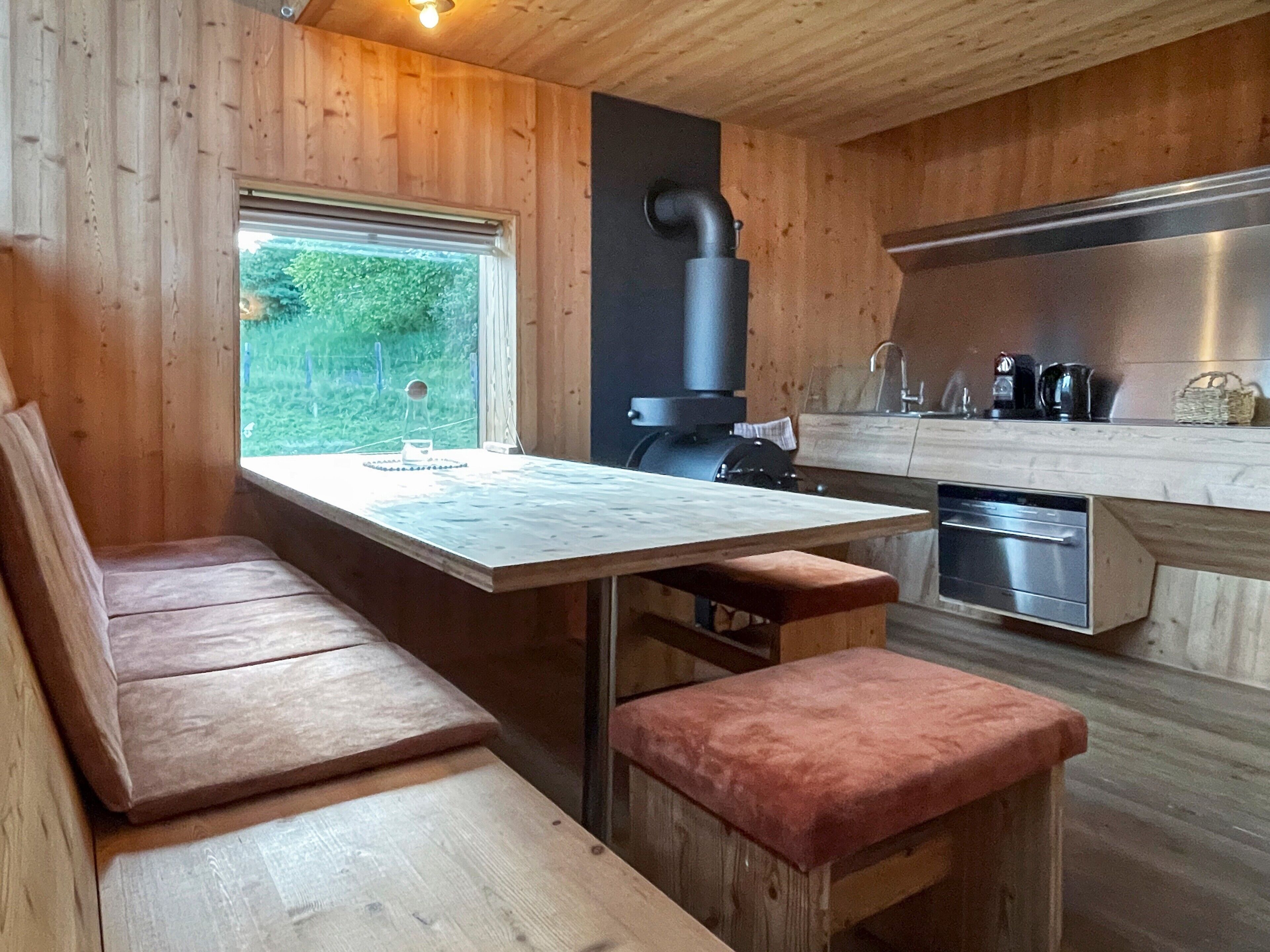 Een houten interieur met een tafel, een bank en een raam met uitzicht op groen.