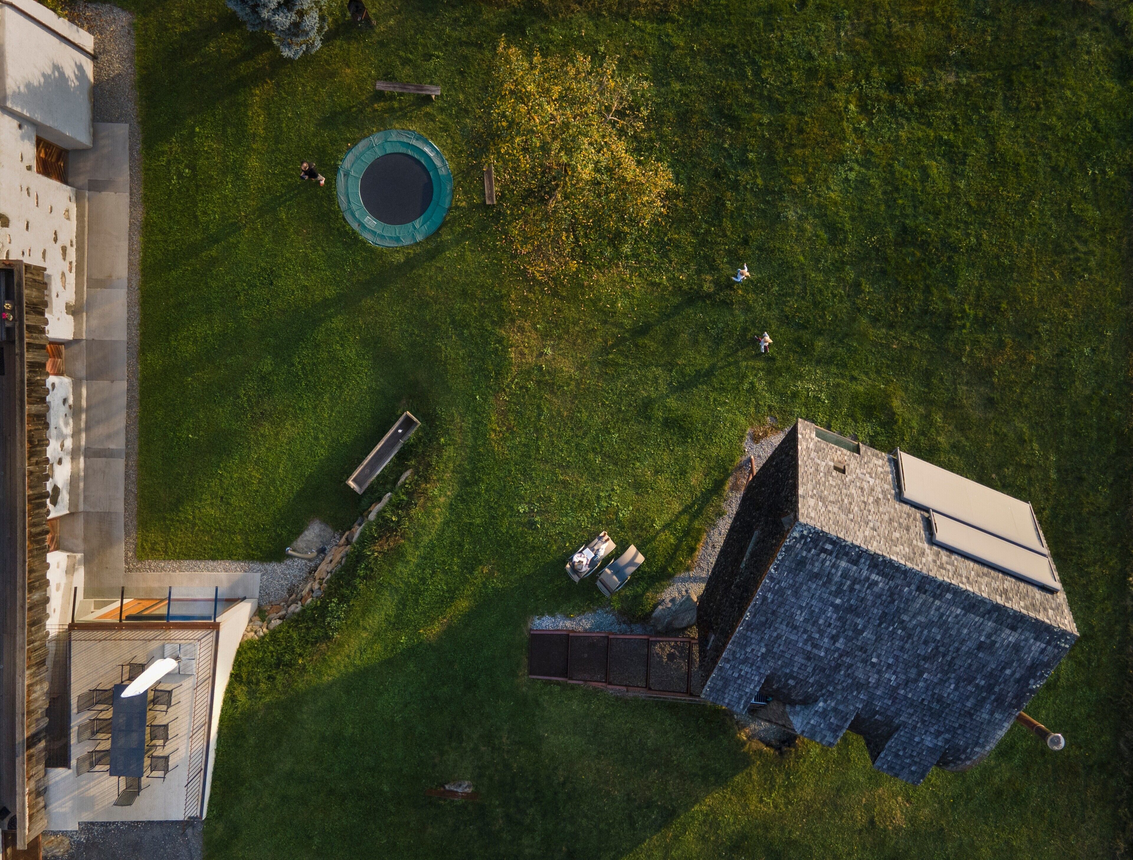 An aerial view of a property with a swimming pool, a patio area with seating, and a building with a sloped roof.