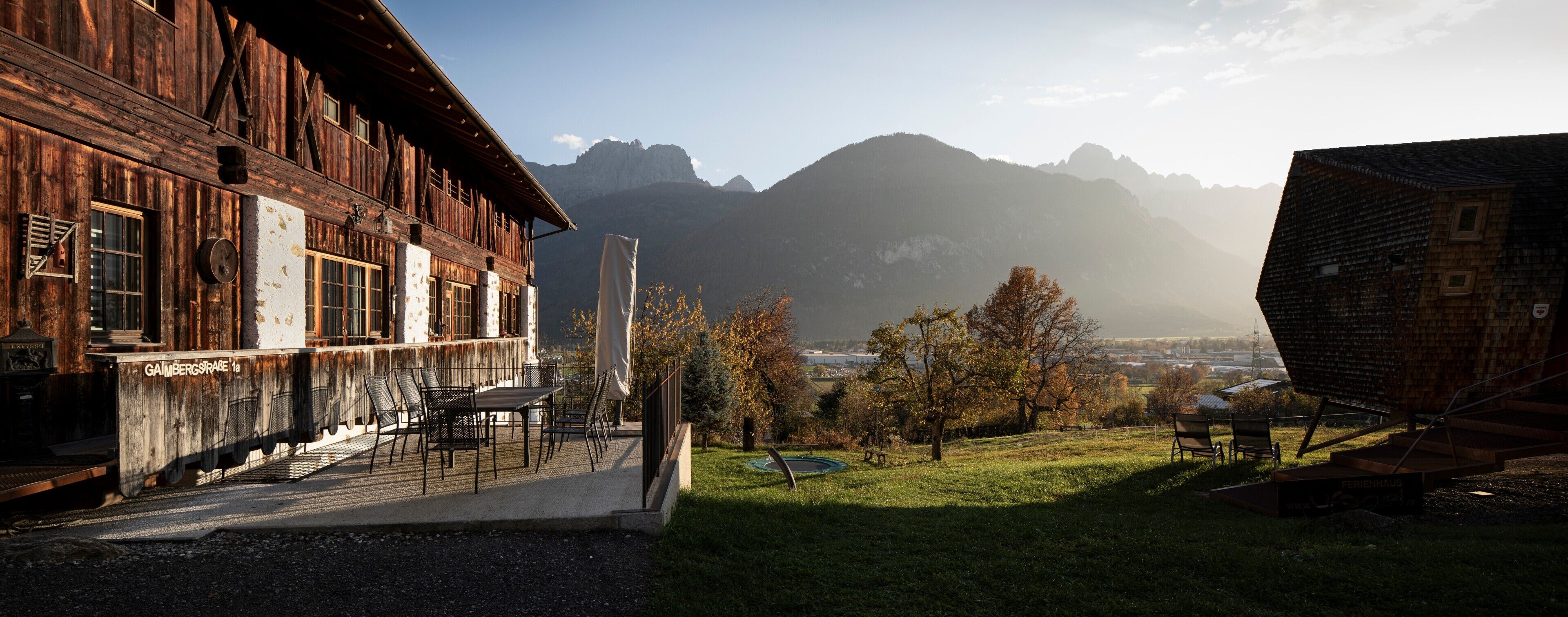 A rustic wooden building with a balcony, a table with chairs, and a view of mountains.