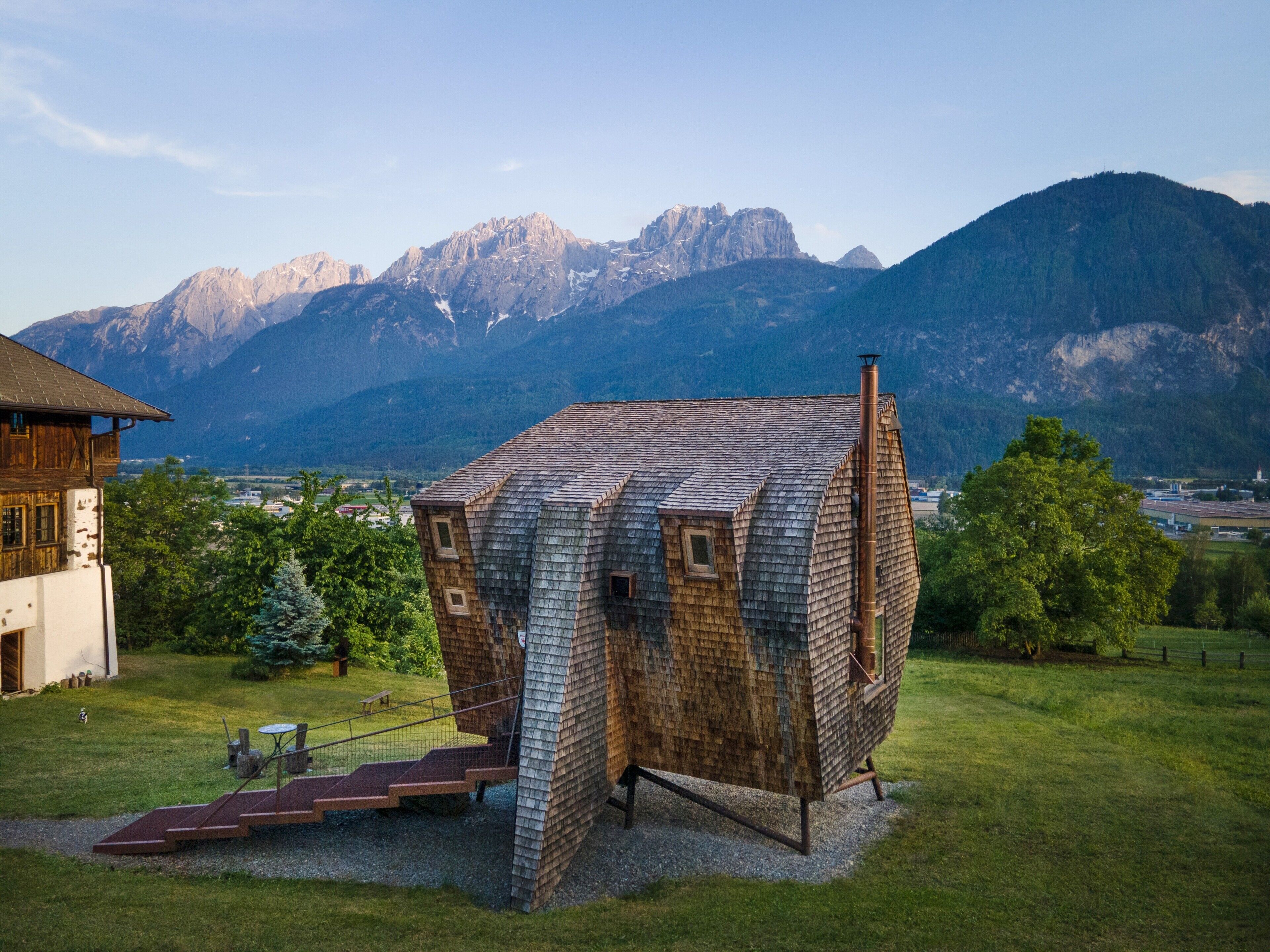 A wooden cabin with a sloped roof, a chimney, and a small staircase leading to a door.