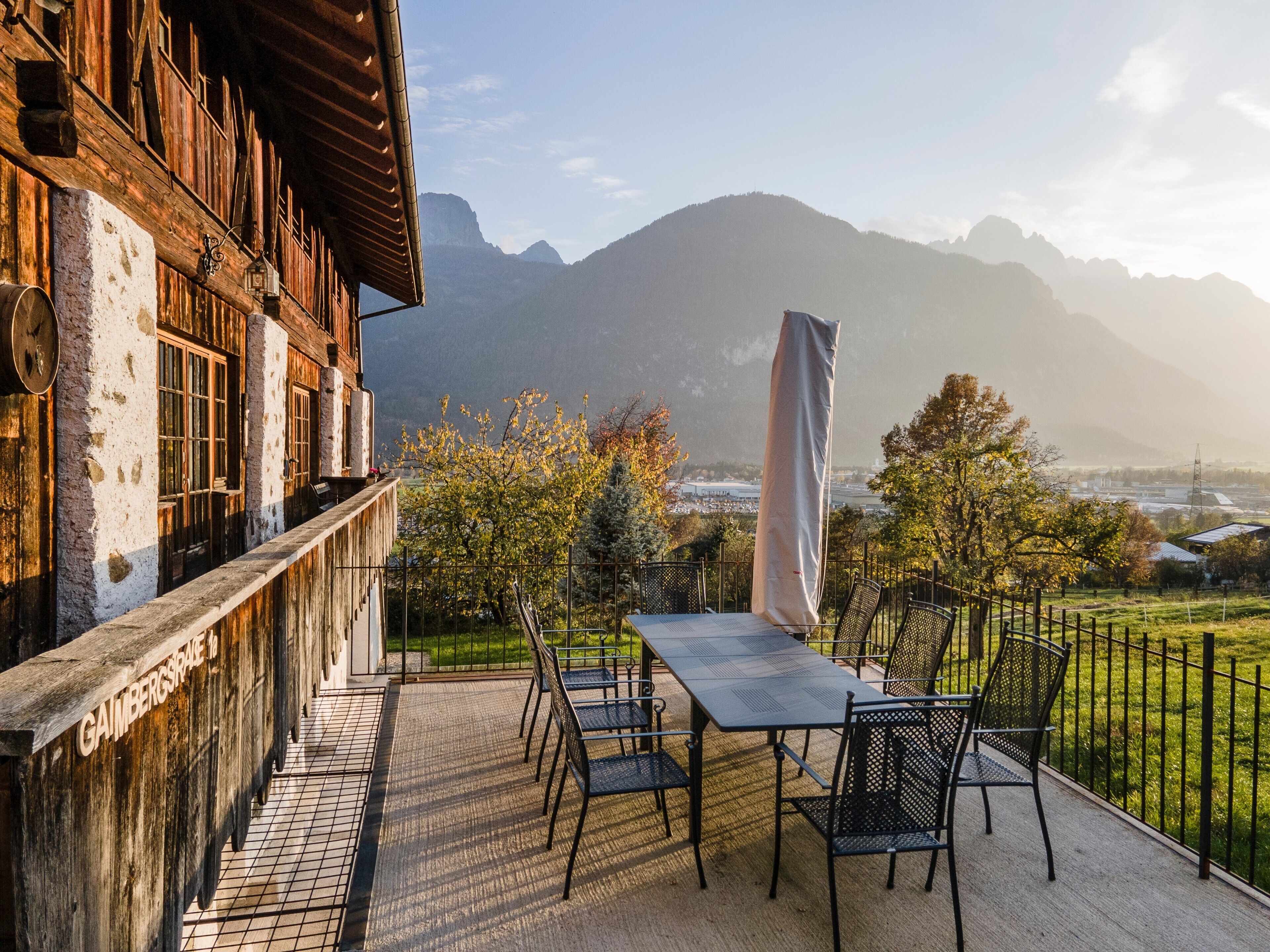 Eine Terrasse mit Tisch und Stühlen, einem schattenspendenden Sonnenschirm und Blick auf Berge.