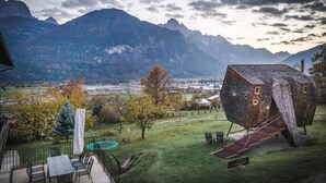 A house with a unique sloped roof design, a patio with outdoor furniture, and a view of mountains in the background.