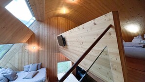 A wooden interior with a bed, a desk, and a window.