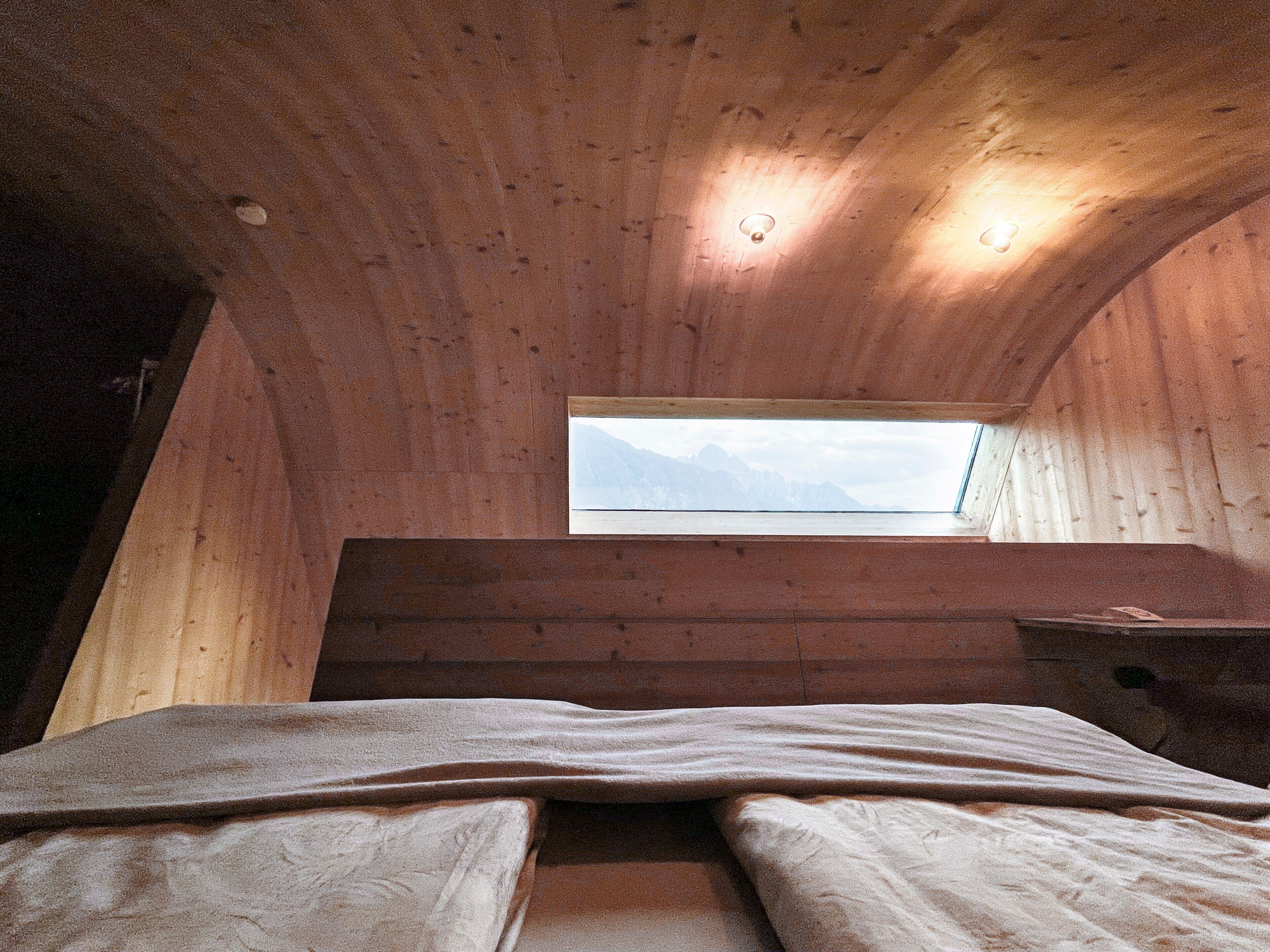 A room with a sloped ceiling, a window with a mountain view, a bed, and a wooden bench.