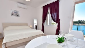 A bedroom with a bed, a dining table with a bowl, a glass, and a plant.