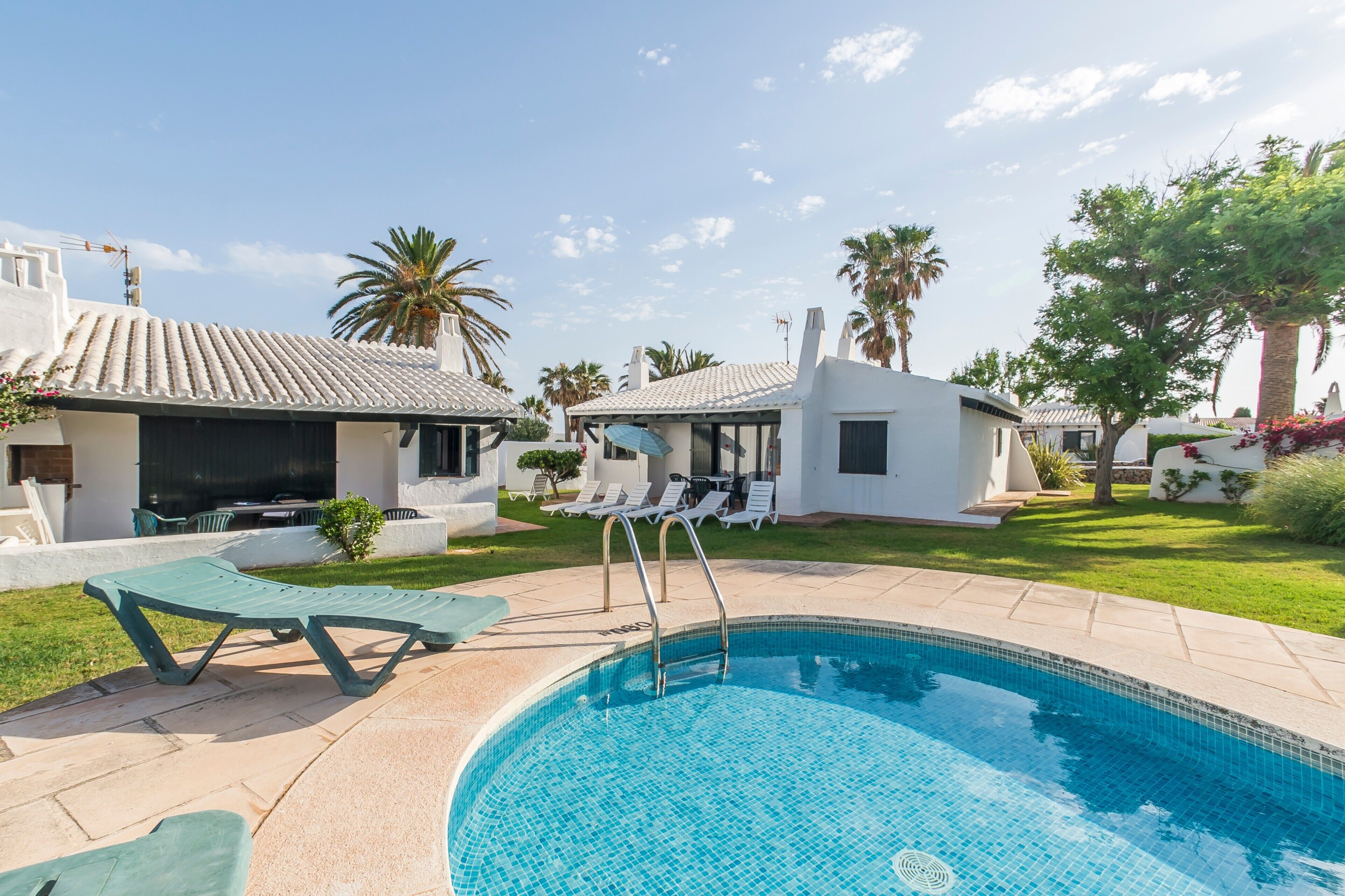 A swimming pool with lounge chairs, a small building, and palm trees.