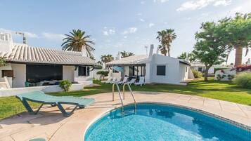 A swimming pool with lounge chairs, a small building, and palm trees.