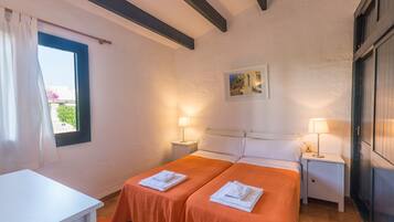 A hotel room with two beds, a desk, a window with curtains, a painting on the wall, and two bedside lamps.