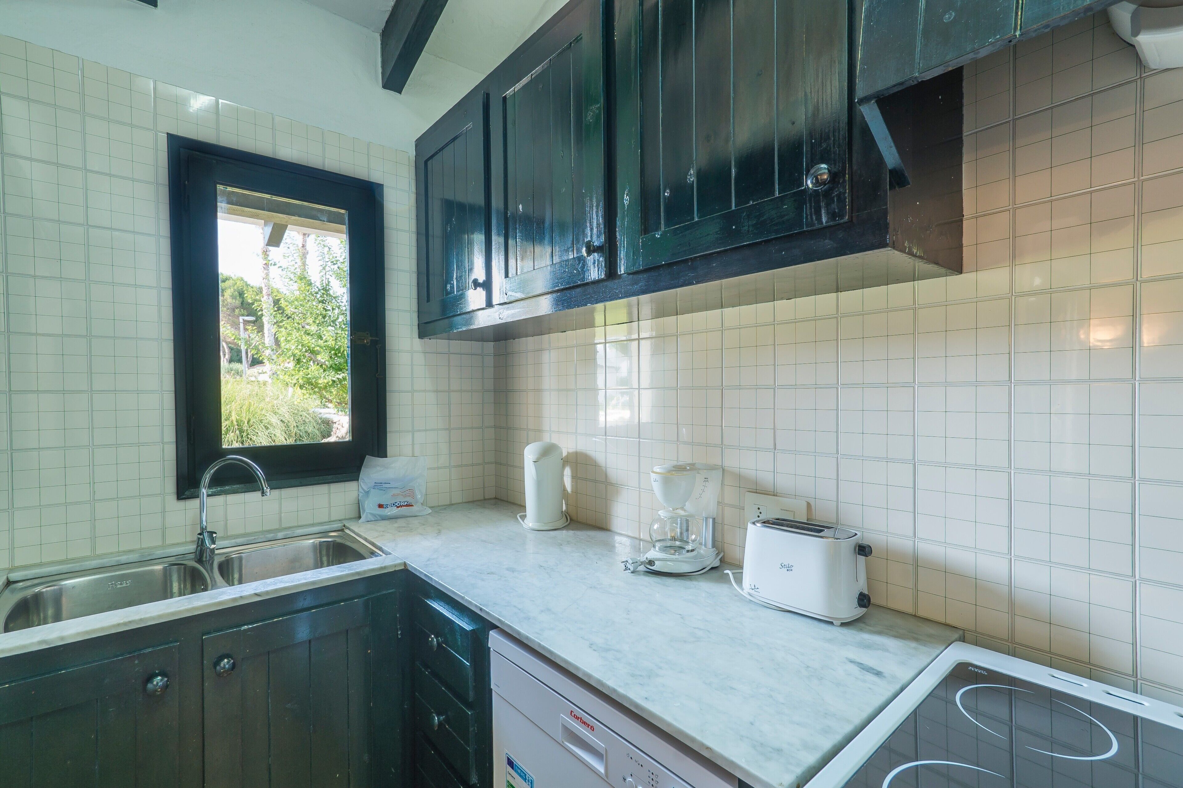 A kitchen with a sink, a coffee maker, a toaster, and cabinets.