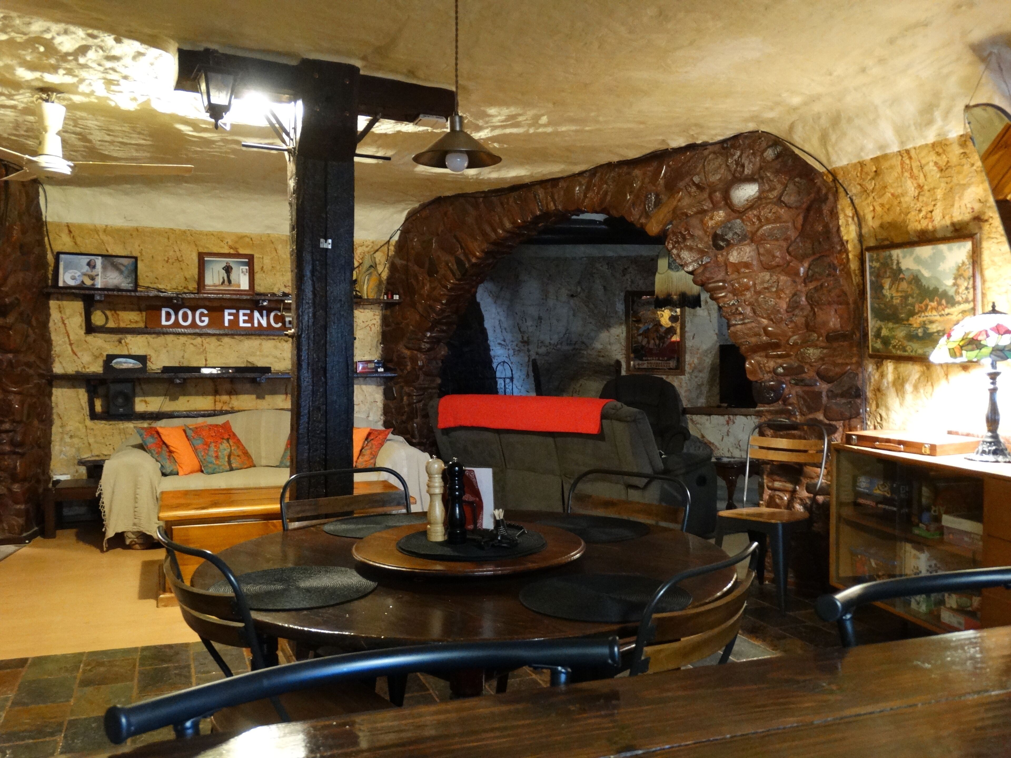 A cozy interior with a stone archway, a dog-themed sign, a fireplace, and a dining area with a round table and chairs.