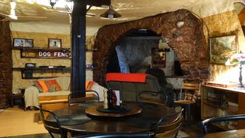A cozy interior with a stone archway, a dog-themed sign, a fireplace, and a dining area with a round table and chairs.