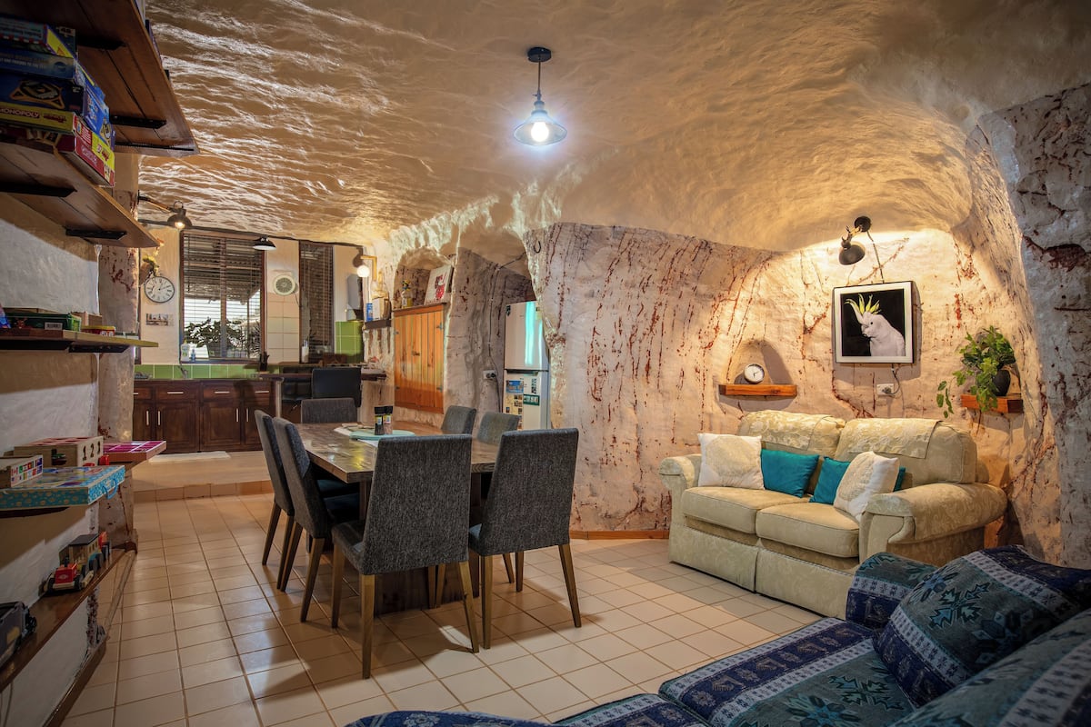 A cozy interior with a dining area, kitchen, and living space, featuring a rustic stone wall and wooden furniture.