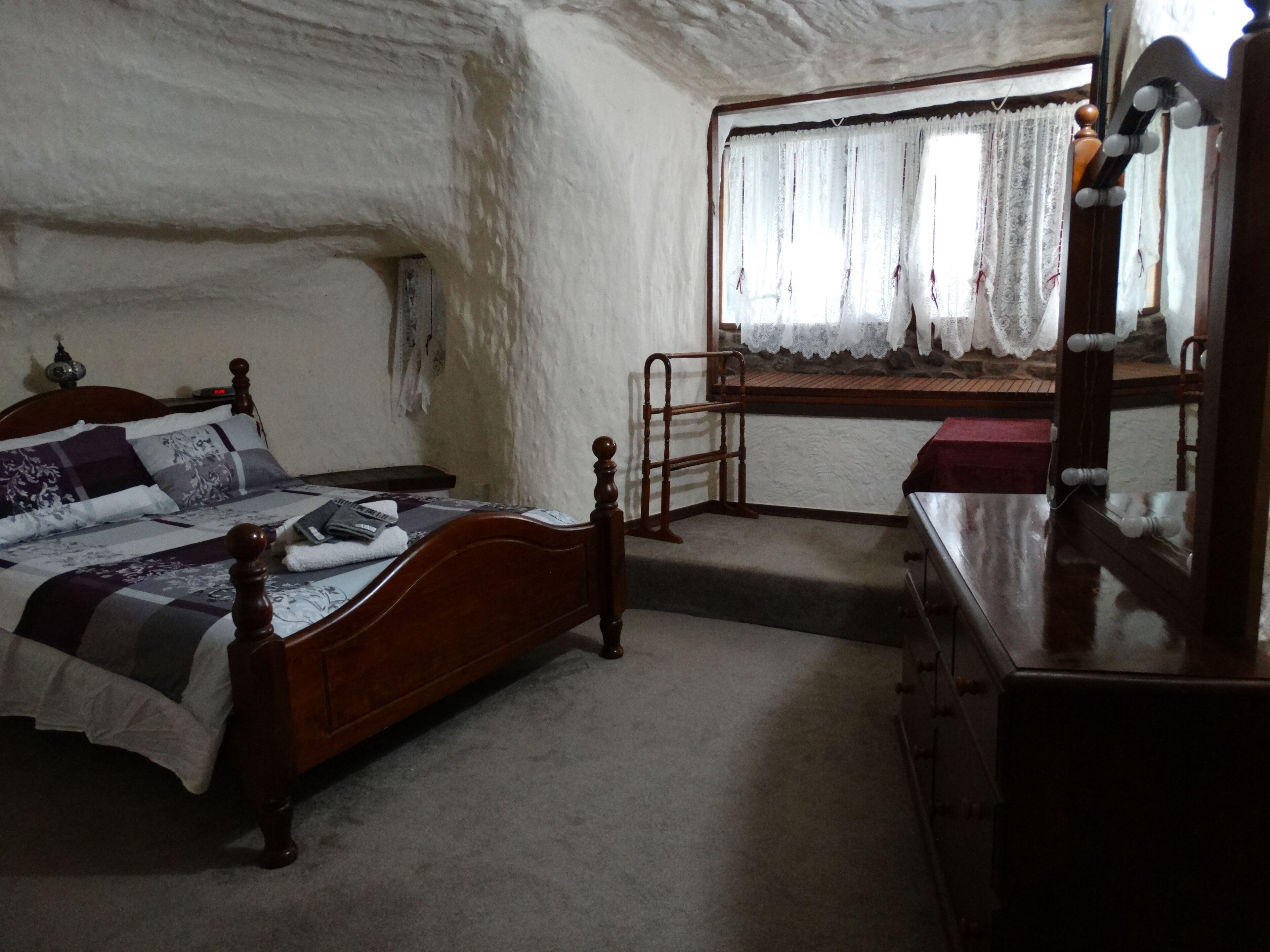 A bedroom with a wooden bed, a dresser, a mirror, and a window with curtains.