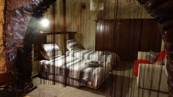 A rustic room with a bed, a chair, and a wooden archway.