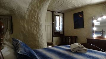 A bedroom with a bed, a wooden headboard, a nightstand, a mirror, and a window with a view of the outside.