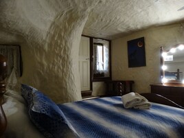 Un dormitorio con cama, cabecera de madera, mesita de noche, espejo y ventana con vistas al exterior.