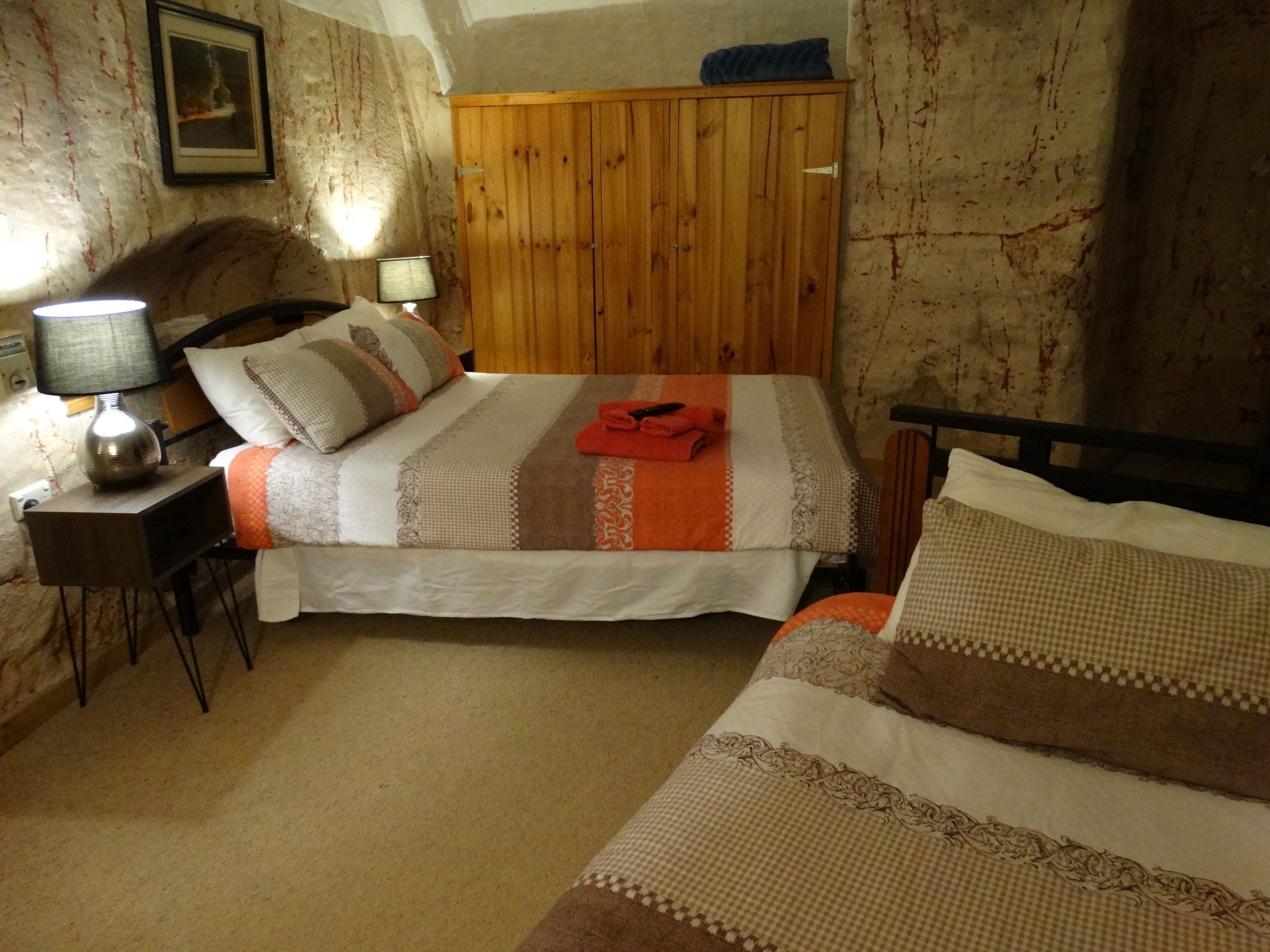 A bedroom with a wooden wardrobe, a bedside table with a lamp, and a bed with striped bedding.