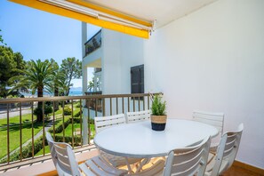 Un balcon avec une table et des chaises blanches, une plante en pot et une vue sur un immeuble et de la verdure.