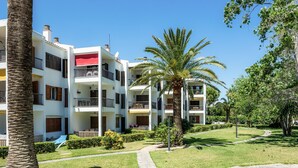 A multi-story hotel with balconies, a well-maintained lawn, and palm trees.