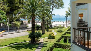 A hotel with a balcony, a view of the beach, and a well-maintained garden.