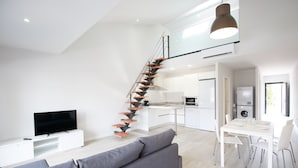 A modern apartment with a staircase, a living room with a sofa and TV, a kitchen, and a dining area. - Estudis Laura (Castell-Platja d'Aro)