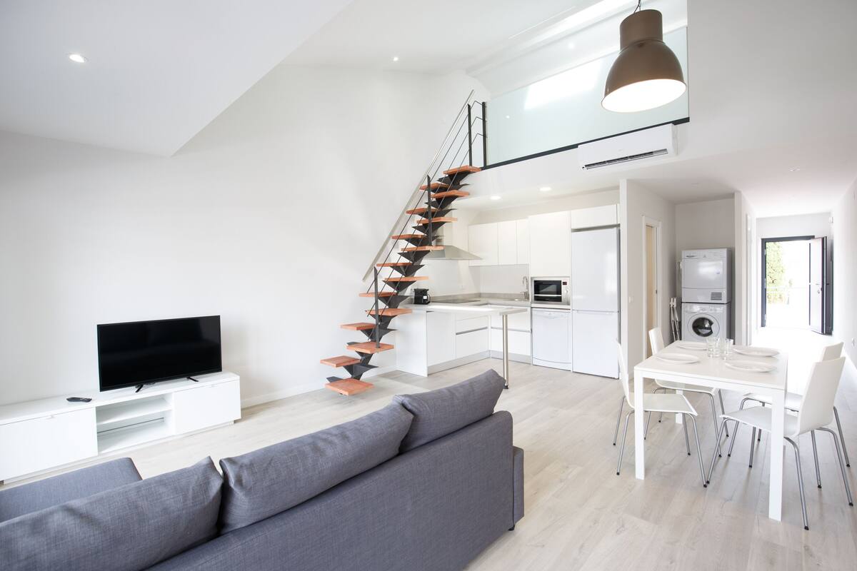 A modern apartment with a staircase, a living room with a sofa and TV, a kitchen, and a dining area.