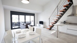 A modern kitchen with white cabinets, a built-in stove, and a staircase with wooden steps. - Estudis Laura (Castell-Platja d'Aro)