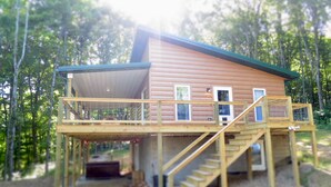 A wooden cabin with a deck and stairs, surrounded by trees. - Rocky Pine Cabin. Hot Tub, and Pet Friendly! (Nelsonville)