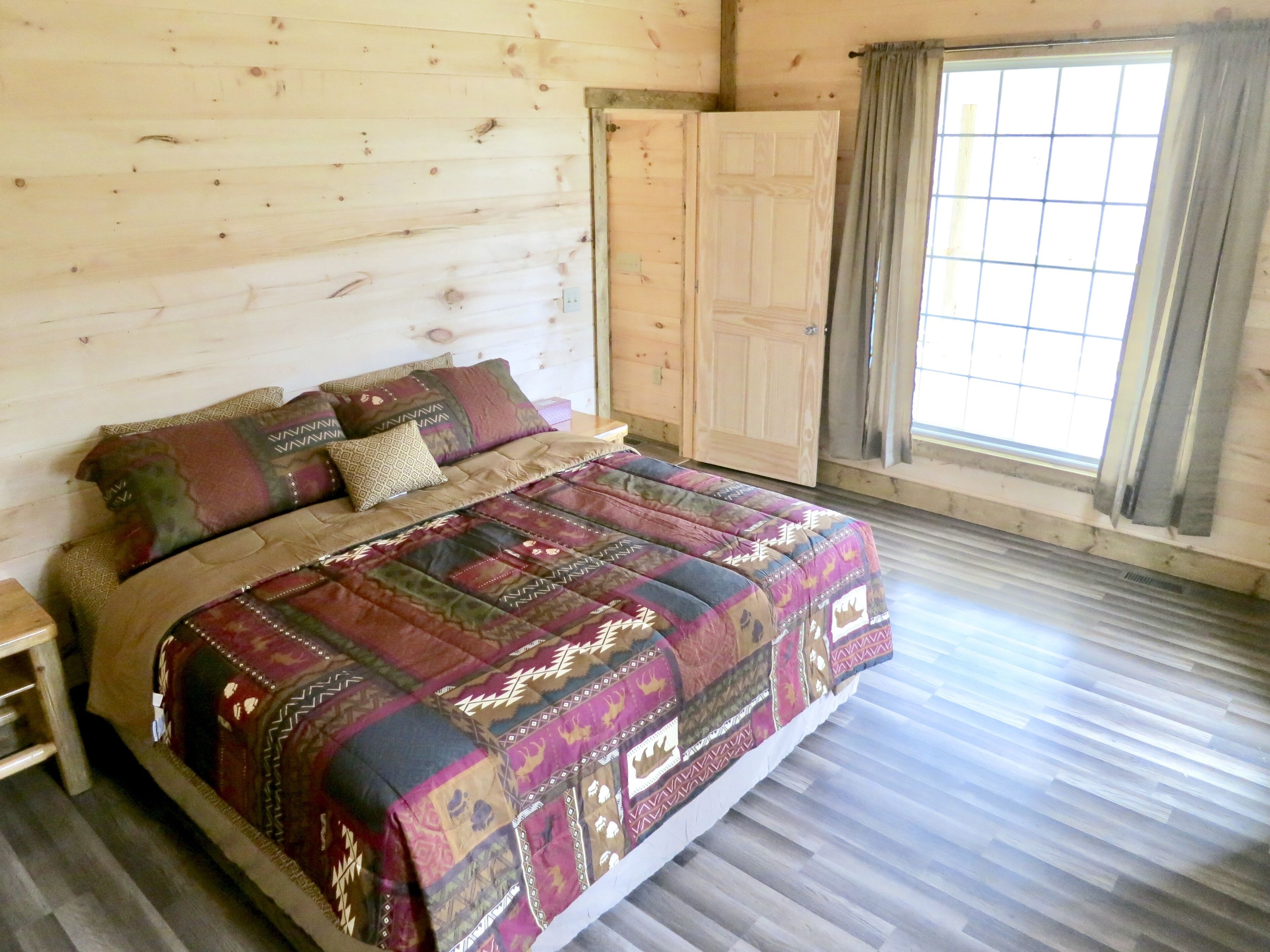 A wooden-paneled bedroom with a bed, a window with curtains, and a wardrobe.