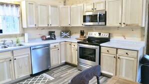 A compact kitchen with wooden cabinets, a stainless steel microwave, a stove, and a dishwasher. - Rocky Pine Cabin. Hot Tub, and Pet Friendly! (Nelsonville)