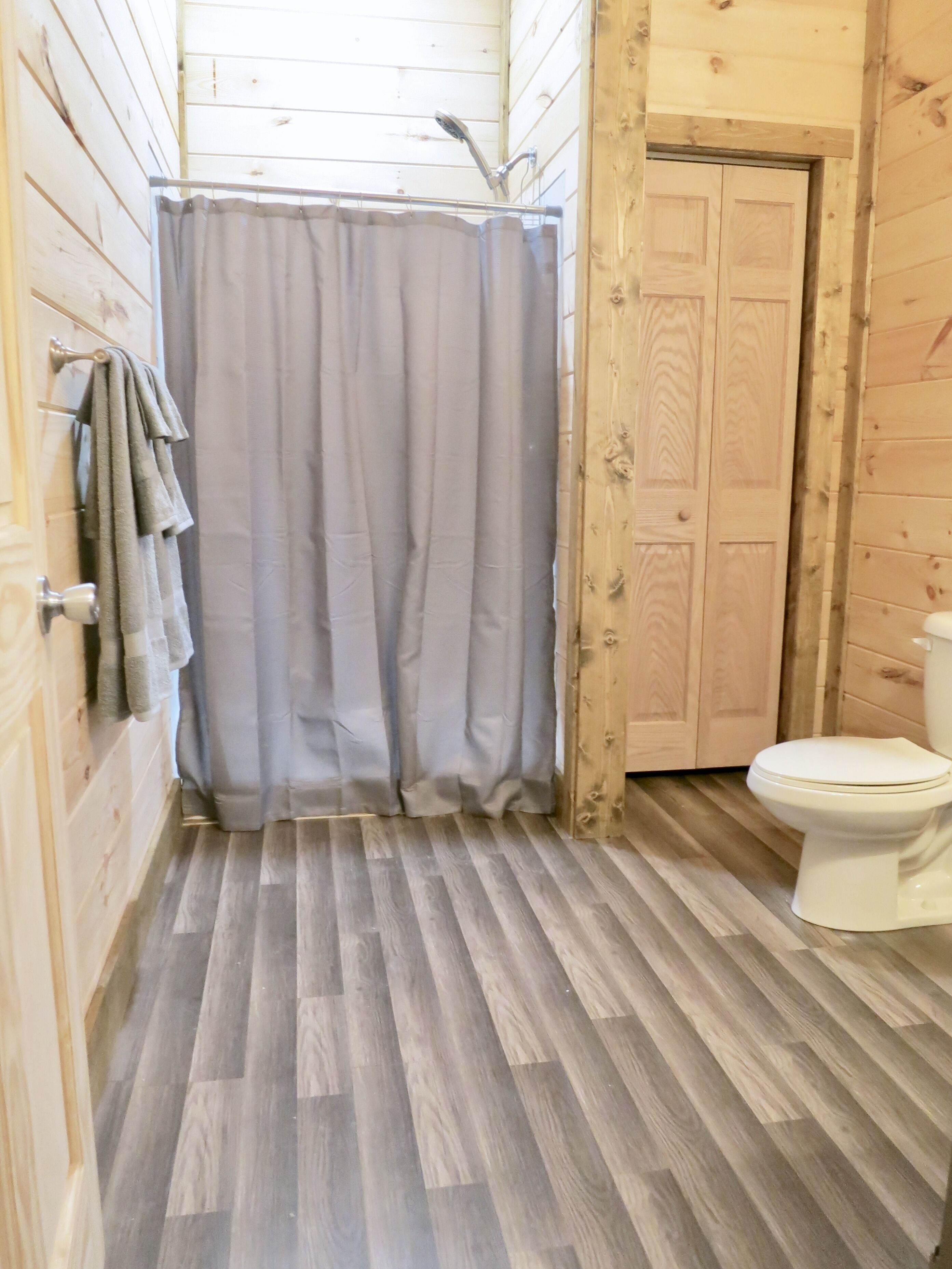 A bathroom with a shower curtain, wooden walls, a toilet, and a towel rack.