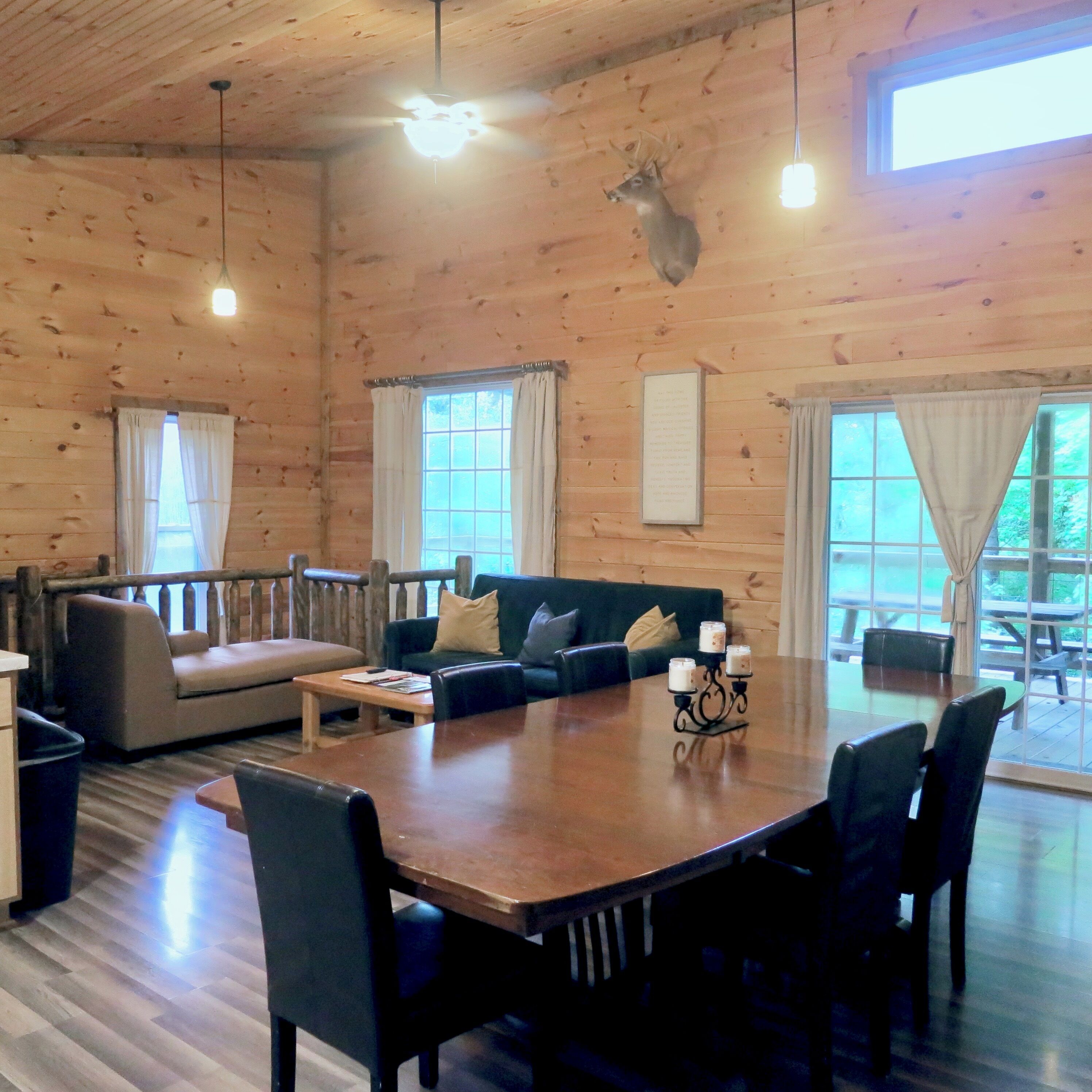 A wooden interior with a dining table, chairs, a sofa, and a ceiling fan.