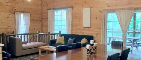 A wooden interior with a dining table, chairs, a sofa, and a ceiling fan.